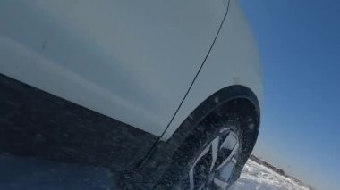 Traveling by car in winter. Close-up on the right front wheel of the SUV. The littered horizon is like a dynamic reception. A white car is driving through a snowy field. An exciting road adventure.