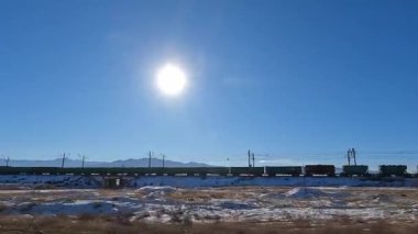 View of a long moving train with freight cars. The train is traveling in the mountains of Kyrgyzstan. A sunny day. An exciting road adventure.