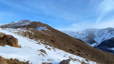 Walk in the mountains in winter. Snow-covered slopes, mountain ranges and peaks. Blue sky and white clouds. Journey through amazing Kyrgyzstan.
