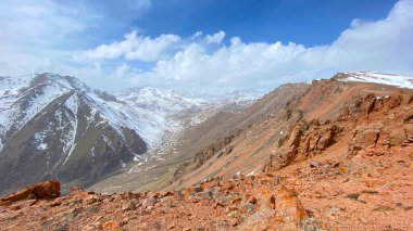 Kızıl kayalıklardan ve karlı dağlardan oluşan bir panorama. Mavi gökyüzü ve beyaz bulutlar. Kırgızistan 'ın inanılmaz doğası. İnanılmaz bir dağ manzarası. Doğal sakin arkaplan.
