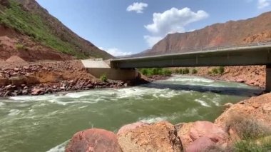 Fırtınalı bir dağ nehri köprünün altından akar. Dağlarda pitoresk bir vadi. Büyük kayaları olan bir köprü. Kırgızistan 'ın inanılmaz doğası.