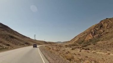 Dağların manzarası, yeşil tepeler, tepeler ve asfalt yol. Kırgızistan 'da minivanla seyahat ediyor. Güzel çöl dağ manzarası. Heyecanlı bir yol macerası.