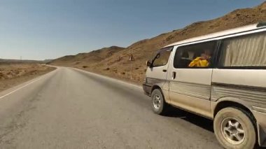 Heyecanlı bir yol macerası. Kırgızistan 'da minivanla seyahat ediyor. Dağların manzarası, yeşil tepeler, tepeler ve asfalt yol. Güzel çöl dağ manzarası.