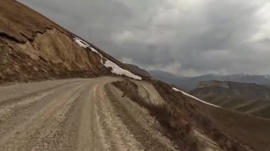 Kırgızistan 'da arabayla seyahat ediyor. Dağ yolunda bir yılan gezisi. Kayalık dağlar, yeşil tepeler ve toprak kayalık yol manzarası. Heyecan verici bir yolculuk..