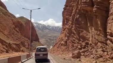 Minibüs iki yüksek kayanın arasından geçiyor. Güzel dağ vadisi. Renkli kayalar, yeşil tepeler, bir köy ve karlı dağlar. Kırgızistan 'da heyecanlı bir yol macerası.