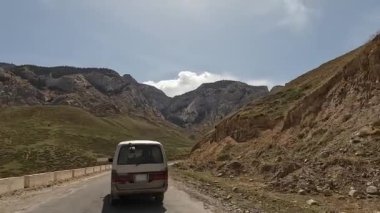 Güzel bir dağ vadisine doğru giden bir minivanın arka görüntüsü. Yüksek uçurumlar ve yeşil tepeler. Kırgızistan 'da heyecanlı bir yol macerası. Arabayla seyahat..