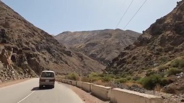 Güzel bir dağ geçidinden geçen bir minivanın arka görüntüsü. Dağların, kayaların ve nehrin manzarası. Kırgızistan 'da heyecanlı bir yol macerası. Arabayla seyahat..