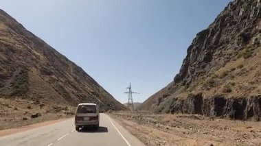 Güzel bir dağ yolunda giden bir minivan. Kırgızistan 'da heyecanlı bir yol macerası. Tepeler, kayalar ve dağ nehri manzarası. Arabayla seyahat..
