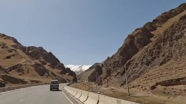Minivan yüksek kayalık dağları geçerek güzel bir dağ yolu boyunca ilerliyor. İnanılmaz bir dağ manzarası. Kırgızistan 'da heyecanlı bir yol macerası.