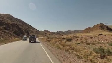 Issız bir dağ yolunda bir minivan yolculuğu. Arabanın penceresinden dağlara ve tepelere bakın. Kırgızistan 'da arabayla seyahat ediyor. Heyecanlı bir dağ yolu macerası.