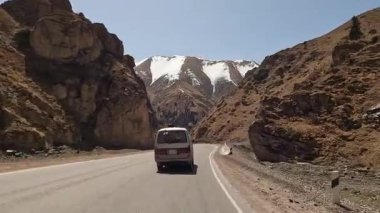 Minivan harika bir dağ geçidinden geçiyor. Karla kaplı dağların, kayaların ve tepelerin manzarası. Kırgızistan 'da heyecanlı bir yol macerası. Kırgızistan 'da arabayla seyahat etmek.