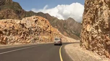 Kırgızistan 'da arabayla seyahat ediyor. Yol boyunca giden bir minivanın arka görüntüsü, görkemli çok renkli dağlar ve yeşil tepeler arasında. Heyecanlı bir dağ yolu macerası.