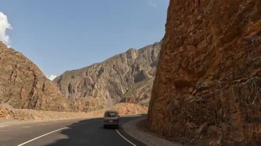 Minivan, görkemli çok renkli dağlar ve yeşil tepeler arasında harika bir yol boyunca ilerliyor. Heyecan verici bir dağ yolu macerası. Kırgızistan 'da arabayla seyahat etmek.