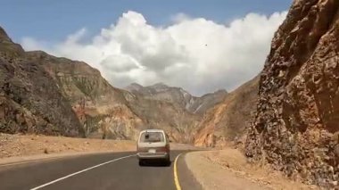 Yol boyunca giden bir araba manzarası, görkemli çok renkli dağlar ve yeşil tepeler arasında. Heyecan verici bir dağ yolu macerası. Kırgızistan 'da arabayla seyahat etmek.