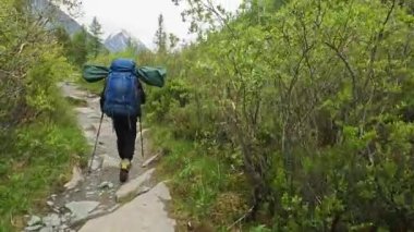 Büyük sırt çantalı yalnız bir turist ormanda kayalık bir patika boyunca yürüyor. Belukha 'nın tepesine doğru yürü. Altai, Rusya 'nın şaşırtıcı doğası. Yeşil parkta bir yürüyüş..