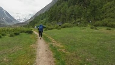 Yeşil parkta yürü, ağaçları, çalıları ve karlı dağları geç. Büyük bir sırt çantalı bir dağcı patika boyunca yürüyor. Belukha 'ya tırmanmak. Altai, Rusya 'nın güzel doğası.