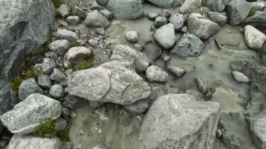 Yürüyüş direkleri olan bir turist sığ bir dağ deresinde kayaların üzerinde yürüyor. Bacakların aşağıya doğru birinci şahıs görüntüsü. Belukha 'ya tırmanmak. Altai, Rusya 'nın güzel doğası.