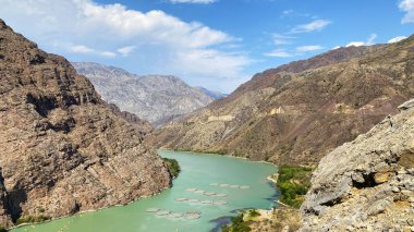 Kırgızistan 'ın kayalık dağlarındaki mavi Naryn Nehri. Nehirde balık yetiştirmek için kullanılan kompartımanların manzarası. Dağlar, tepeler, kırgızistan 'ın tepeleri ve kayaları. Sakin doğal arka plan. Güzel dağ manzarası.