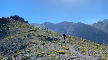 Bir grup turist yokuş yukarı yürüyor. Ala-Archa Ulusal Parkı, Kırgızistan. Dağ tepeleri, kayalar ve yamaçlar görünüyor. Güzel dağ yaz manzarası. Sakin doğal arka plan.