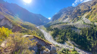 Kırgızistan 'daki Ala Archa Ulusal Parkı' ndaki bir dağ nehrinin manzarası. Güzel dağ manzarası. Dağlarda güneşli bir gün. Aktif yaz tatili. Yeşil tepelerin, yamaçların, kayaların, tepelerin ve dağların muhteşem manzarası.