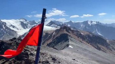 Kırgızistan bayrağı Komsomolets Tepesi 'nin tepesinde dalgalanıyor. Ala-Archa Ulusal Parkı, Kırgızistan. Kırgız sırtının karlı dağları, kayaları, yamaçları ve tepeleri.