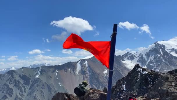 山顶是科莫洛茨峰 吉尔吉斯斯坦的国旗在风中飘扬 吉尔吉斯斯坦阿拉阿卡国家公园 吉尔吉斯斯坦山岭的白雪覆盖的山脉 斜坡和山峰 — 图库视频影像