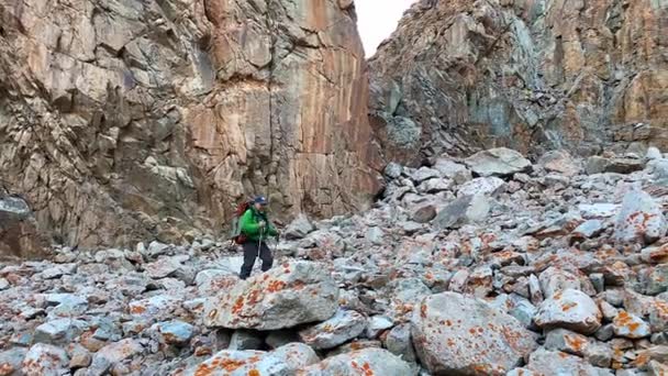大きなバックパックとトレッキングポールを持つ男は 高い岩の崖の近くの山を歩いています アルチャ国立公園 キルギス 山でのアクティブな夏休み 美しい山の風景 — ストック動画