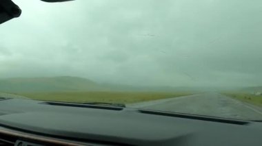 Şiddetli yağmurda arabayla seyahat etmek. Arabanın çalışan sileceklerinin görüntüsü. Issız bir bölge. Paved yolu, yeşil tarlalar ve tepeler. Kırgızistan 'ın inanılmaz doğası.