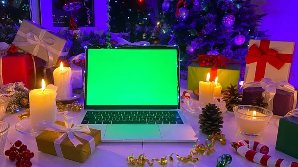 Colorful gift boxes, burning candles, cones, confetti and other elements of Christmas. Beautiful New Year background. Festive New Year\'s table with a laptop with a chroma key on the screen.