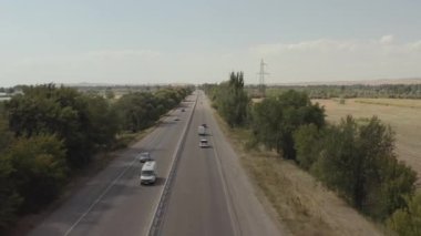 Kırsal bir bölgede asfalt bir yolda arabalar sürüyorlar. Güzel kırsal alan, yeşil ağaçlar, elektrik hattı. Kırgızistan 'da arabayla seyahat ediyor. Yaz tatili.