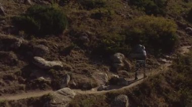 Büyük bir sırt çantası ve yürüyüş direkleri olan bir adam dağ yolunda yürüyüşe çıkar. Uzakta bir grup turist var. Kırgızistan 'daki Ala-Archa Ulusal Parkı. Dağ manzarası. Aktif boş zaman.