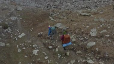 Geniş sırt çantaları ve yürüyüş direkleriyle renkli giysiler içindeki gençler dar kayalık bir dağ yolunda yürüyorlar. Dağlarda aktif bir eğlence. Kırgızistan 'daki Ala-Archa Ulusal Parkı. Güzel manzara.