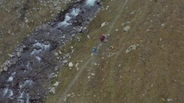 Sırt çantaları ve yürüyüş direkleriyle bir adam ve bir kadın dar bir patika boyunca fırtınalı bir dağ nehri boyunca yürüyorlar. Kırgızistan 'daki Ala-Archa Ulusal Parkı. Dağlarda aktif eğlence..