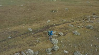 Büyük sırt çantaları ve yürüyüş direkleriyle yalnız bir turist kayalık bir plato boyunca yürüyor. Kırgızistan 'daki Ala-Archa Ulusal Parkı. Dağlarda aktif eğlence..
