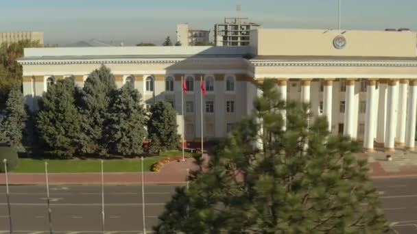 从空中俯瞰吉尔吉斯共和国政府大楼立面的一部分 一座漂亮的建筑 柱子和吉尔吉斯斯坦国旗在风中飘扬 历史和建筑的纪念碑 比什凯克市的行政大楼 — 图库视频影像