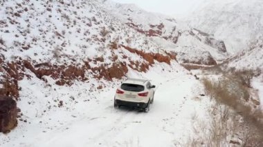 Karlı bir dağ yolunda beyaz bir SUV sürüyor. Arka ve yan görüş. Kızıl dağ kanyonu Konorchek 'in muhteşem manzarası. Kırgızistan 'da arabayla seyahat ediyor. Güzel dağ kış manzarası.