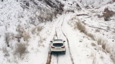Karlı bir dağ yolunda giden beyaz bir cipin arka ve üst görüntüsü. Güzel dağ kış manzarası. Konorchek Kanyonu. Kırgızistan 'da arabayla seyahat etmek.