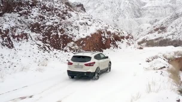 一辆白色的汽车沿着白雪覆盖的山路驶过红坡 Konorchek峡谷 乘坐Suv在吉尔吉斯斯坦旅行 美丽的山地冬季风景 — 图库视频影像
