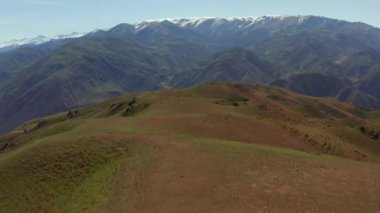 Güneşli bir yaz gününde yeşil tepelerin üzerinde bir dron uçurmak. Uzakta karla kaplı dağ zirveleri. Kırgızistan 'da seyahat. Güzel yaz dağ manzarası.