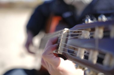 Müzisyen gitar dersleri veriyor. Bir adam gitar çalıyor. Gitarın boynundaki telleri yakın plan çek. Odaklanma, akorları tutan elde. Gitarist rahat bir pozisyonda oturuyor.