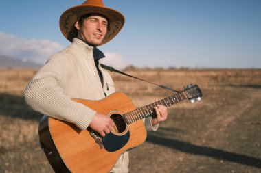 Kovboy şapkalı yalnız bir otantik gitarist cansız bir kuru alanda gitar çalıyor. Kovboy şapkalı ve bej ceketli bir adam elinde gitarıyla bir çiftçinin tarlasında dinleniyor. Müzisyen çalmaktan zevk alırken sahne sakin.