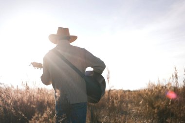 Yalnız bir gitarist gün batımında bir tarlada yürür. Kovboy şapkalı bir adam elinde gitarla kurak direkte yürüyor, arkadan bir manzara. Güneş parıldıyor, sıcak ve davetkar bir atmosfer yaratıyor. Kovboy olanlardan zevk alıyor., 