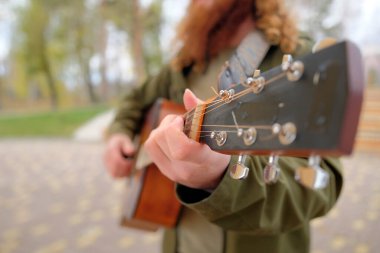 Gitar boynuna yakın çekim, akor tutan bir adamın eline odaklan. Uzun kızıl saçlı bir adam gitar çalar. Gitarist yeşil bir ceket giyiyor. Gitar dersleri