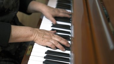 Yaşlı bir piyanistin ellerinin yakın çekimi. Yaşlı bir kadın piyano çalıyor, tüm dikkatler el ve anahtarlarda. Nostalji konsepti ve müziğin güzelliği. Piyano dersleri. Müzik okulu ya da konser.