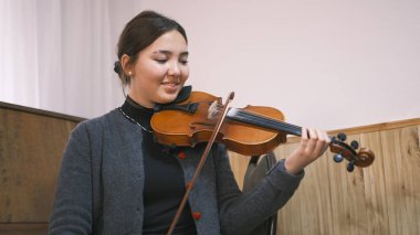 Genç bir Asyalı kadın keman çalmayı öğreniyor. Genç bir kız gülümsüyor ve eğleniyor. Müzik okulunda sınıf öğrencisi. Klasik bir müzik aleti. İlham