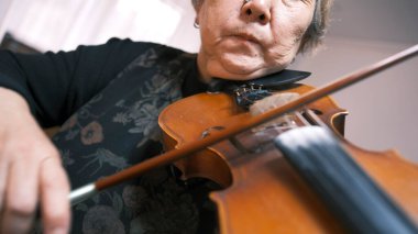 Yaşlı bir Asyalı kadın keman çalıyor, yakın plan, kemancının yüzüne odaklanıyor. Yaşlı, odaklanmış, ilham dolu bir müzisyen, keman üzerine yeni bir melodi besteler. Keman dersleri. Yay.