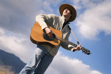 Bir vibe müzisyeni gökyüzüne karşı gitar çalar. Kovboy şapkalı yakışıklı bir adam mavi gökyüzünün altındaki bir tarlada gitar çalıyor. Özgürlük ve yaratıcılık ruhu. Köy hayatı