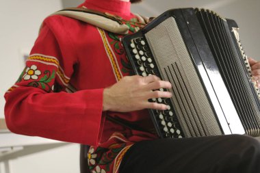 Bir adam akordeon çalıyor. Akordiyoncu ulusal bir kırmızı gömlek ve siyah pantolon giymektedir. Müzisyenin yakın çekimi. Akordiyona odaklan. Akordeon çalma dersleri