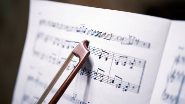 Kemanın yayı notaları gösteriyor, yakın plan. Güzel bir melodisi olan bir nota kağıdı. Müzik okulu. Besteci iş başında. Müzik konsepti ve onun yaratılmasındaki ilhamın önemi