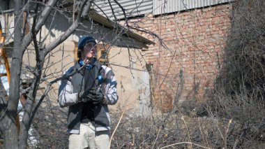 Genç ve çekici bir adam kurak bir bahçede çalışıyor. Bahçenin bahar temizliği. Ağaç buduyorum. Eldiven ve mavi şapka giyiyor. Öğrenciler için yarı zamanlı iş